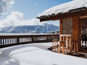 Une terrasse en bois avec une table et des chaises, offrant une vue sur un paysage montagneux enneigé.