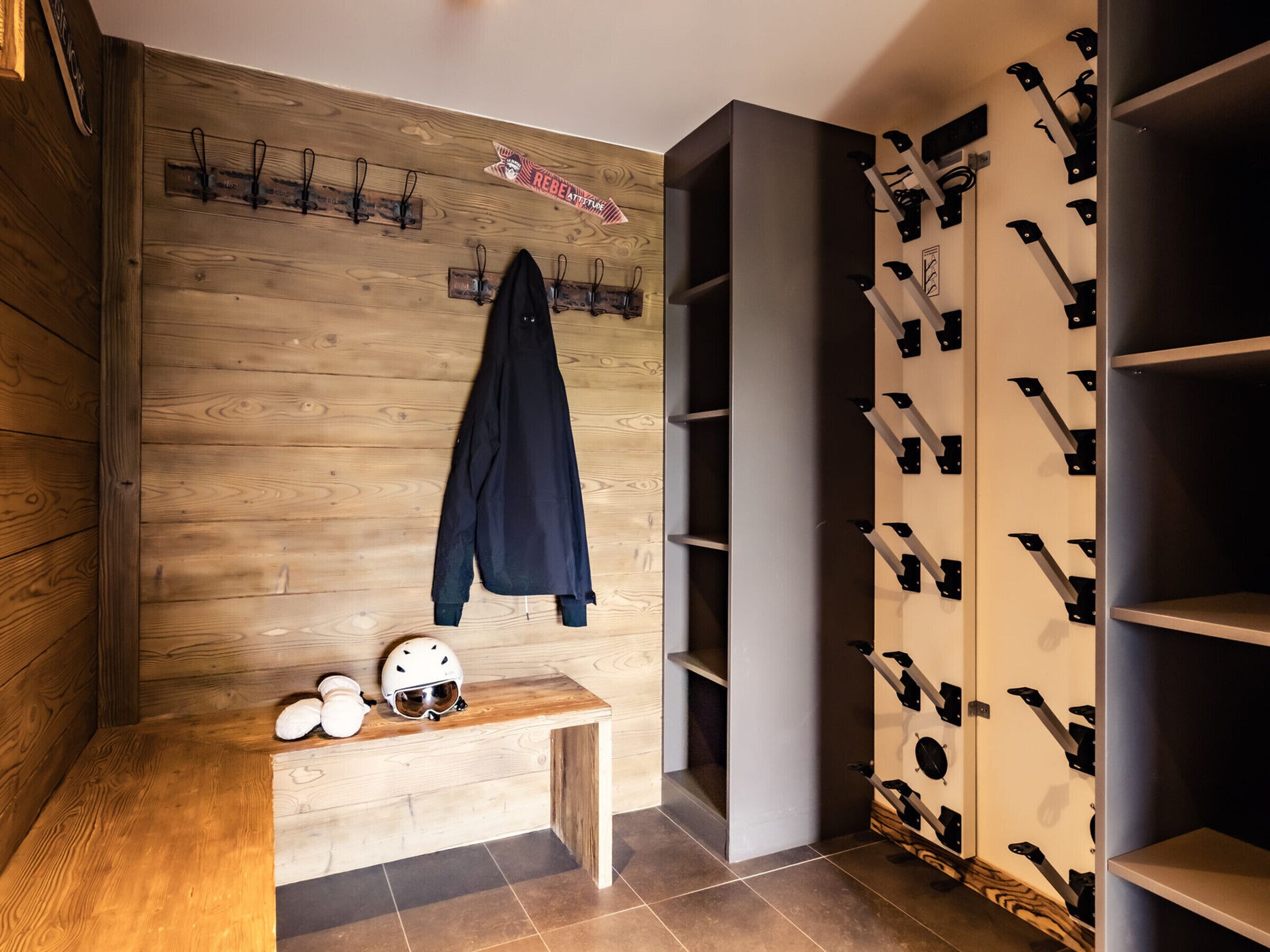 A room with a wooden wall, a bench, a coat rack, and a shoe rack.