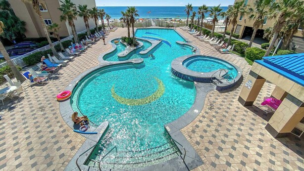 Un área de piscina en un resort con varias piscinas, sillas de descanso y palmeras.