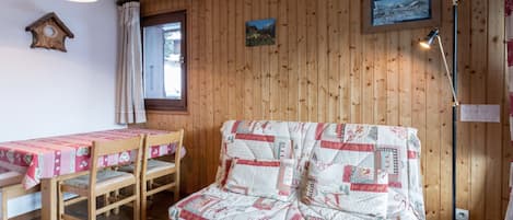 Una habitación acogedora con pared de madera, un sofá acolchado, una mesa de madera con mantel rosa y una lámpara de pie.