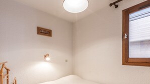 Ein Schlafzimmer mit einem Einzelbett, einer Holzleiter, einer Wandleuchte und einem Fenster mit Jalousien.