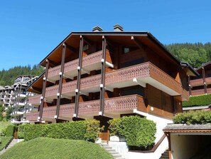 A multi-story wooden building with balconies, surrounded by greenery and a forested hillside.