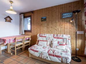 Um quarto aconchegante com parede de madeira, um sofá acolchoado, uma mesa de madeira com toalha de mesa rosa e um abajur.