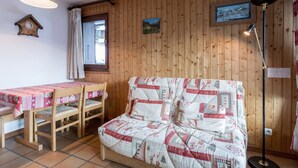 Ein gemütliches Zimmer mit Holzwand, einer gesteppten Couch, einem Holztisch mit rosa Tischdecke und einer Stehlampe.