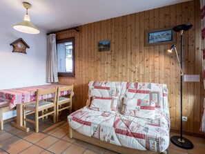 A cozy room with a wooden wall, a quilted sofa, a wooden table with a pink tablecloth, and a floor lamp.