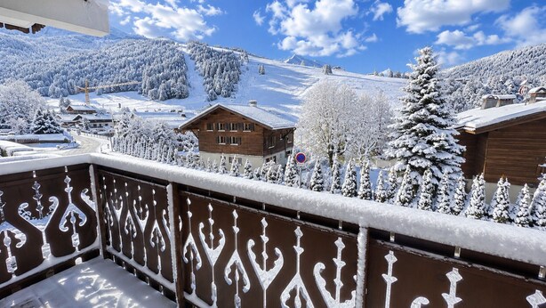 Ein mit Schnee bedeckter Balkon mit Blick auf ein Gebirge und ein Holzhaus.