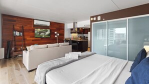 Ett modernt hotellrum med en stor säng, en soffa, ett litet kök och en skjutdörr i glas som leder ut till uteplatsen.