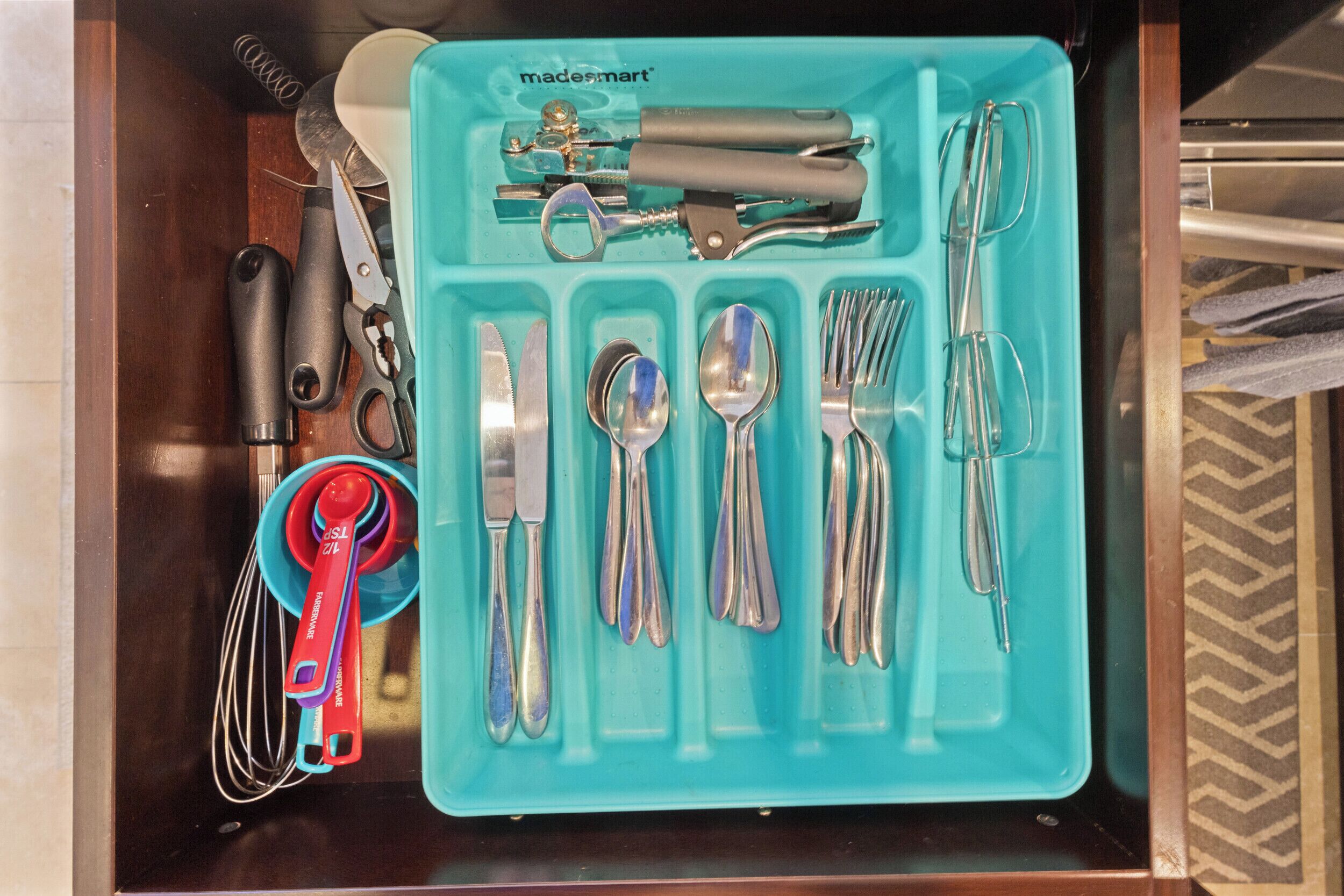 Een lade gevuld met verschillende keukengerei en -tools, waaronder scharen, een mes, lepels, vorken en een garde.