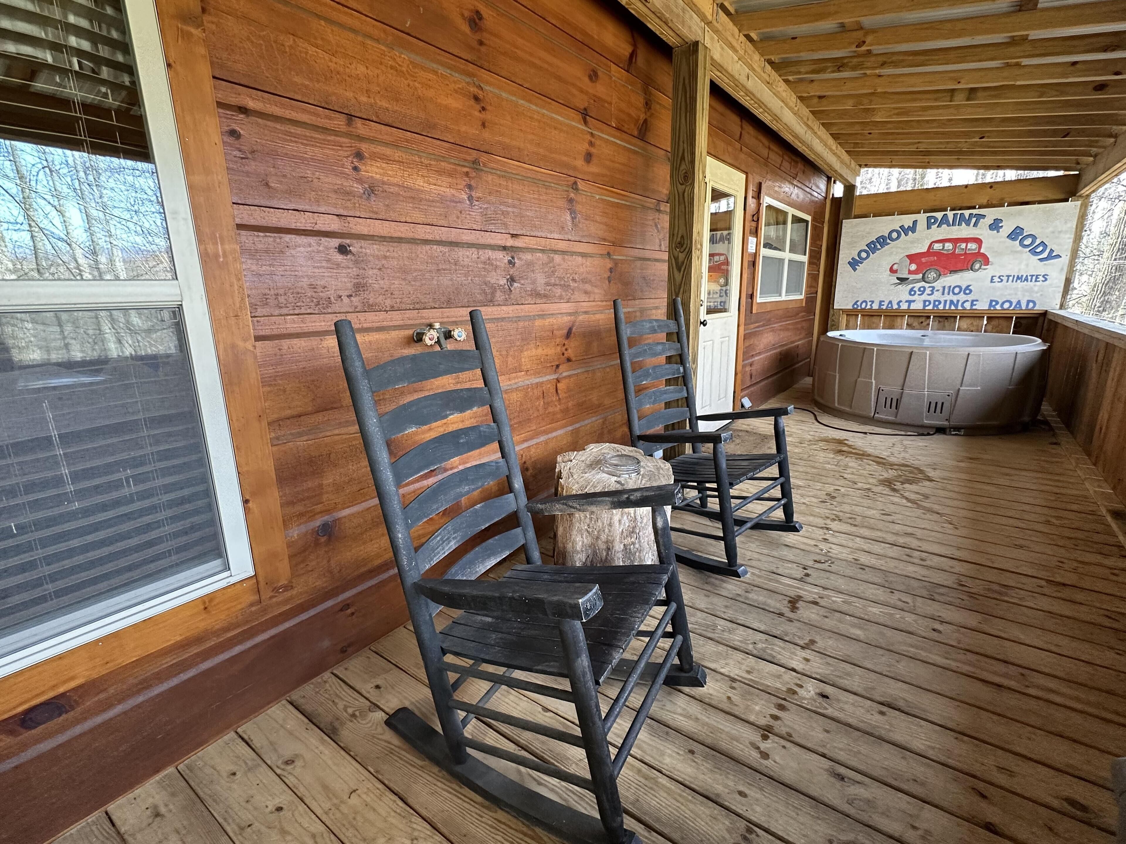 A wooden porch with two rocking chairs, a hot tub, and a wooden wall with a business sign.