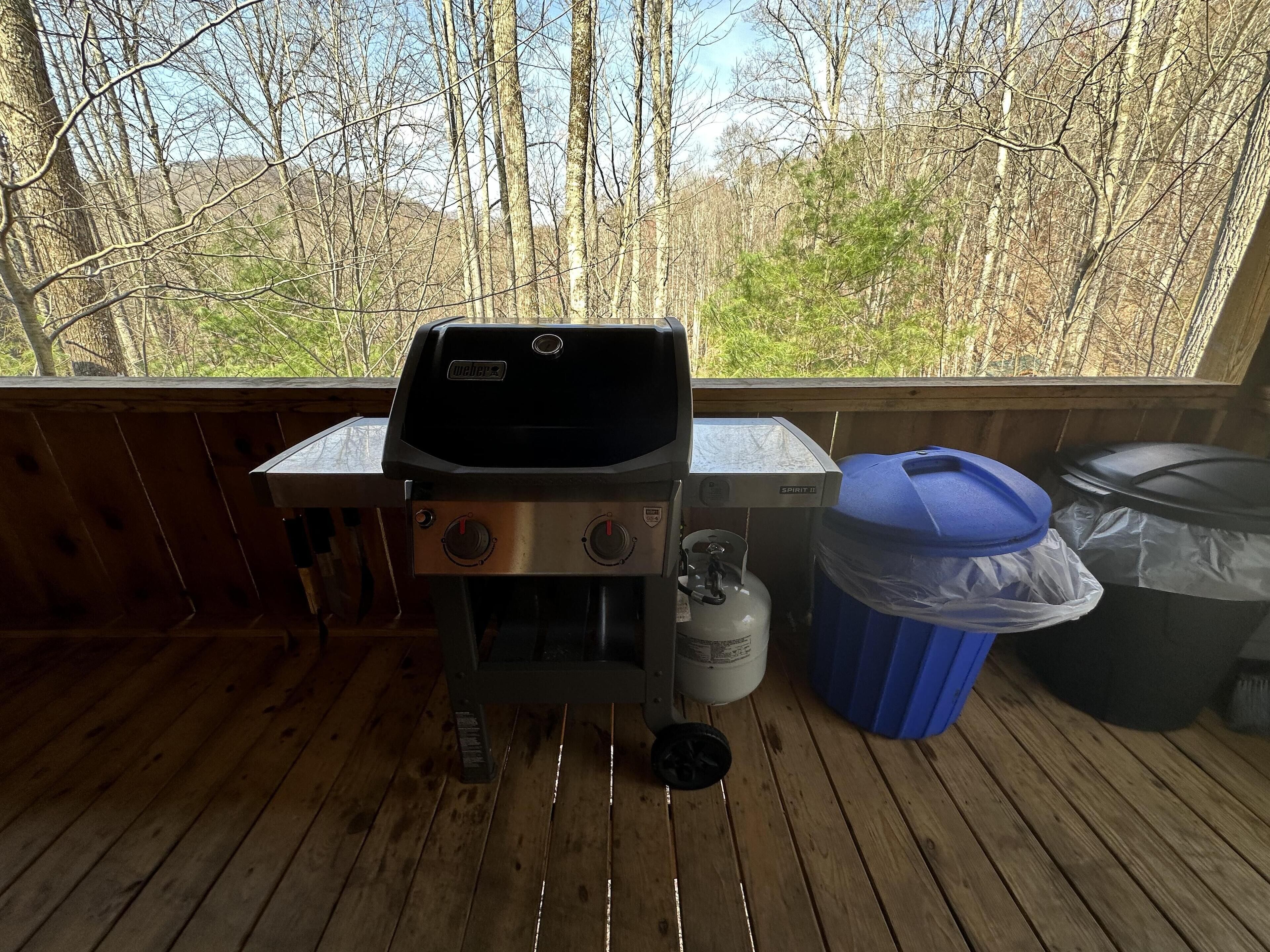 Een houten terras met een gasgrill, een propaanfles en vuilnisbakken.