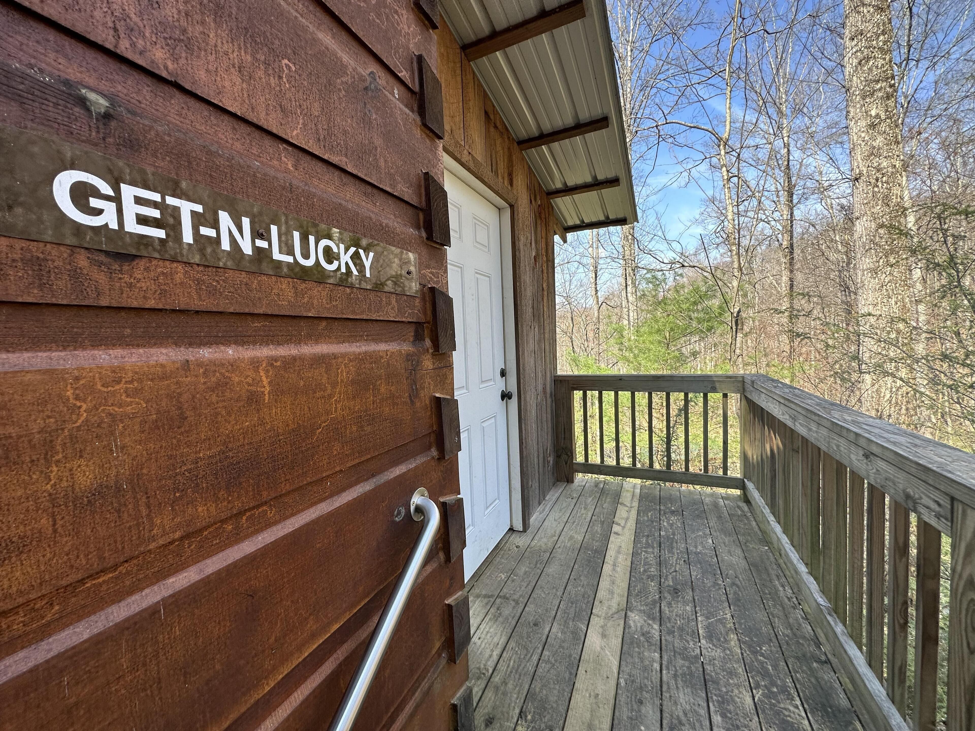 A wooden cabin with a sign reading "GET-N-LUCKY" and a wooden deck leading to a white door.