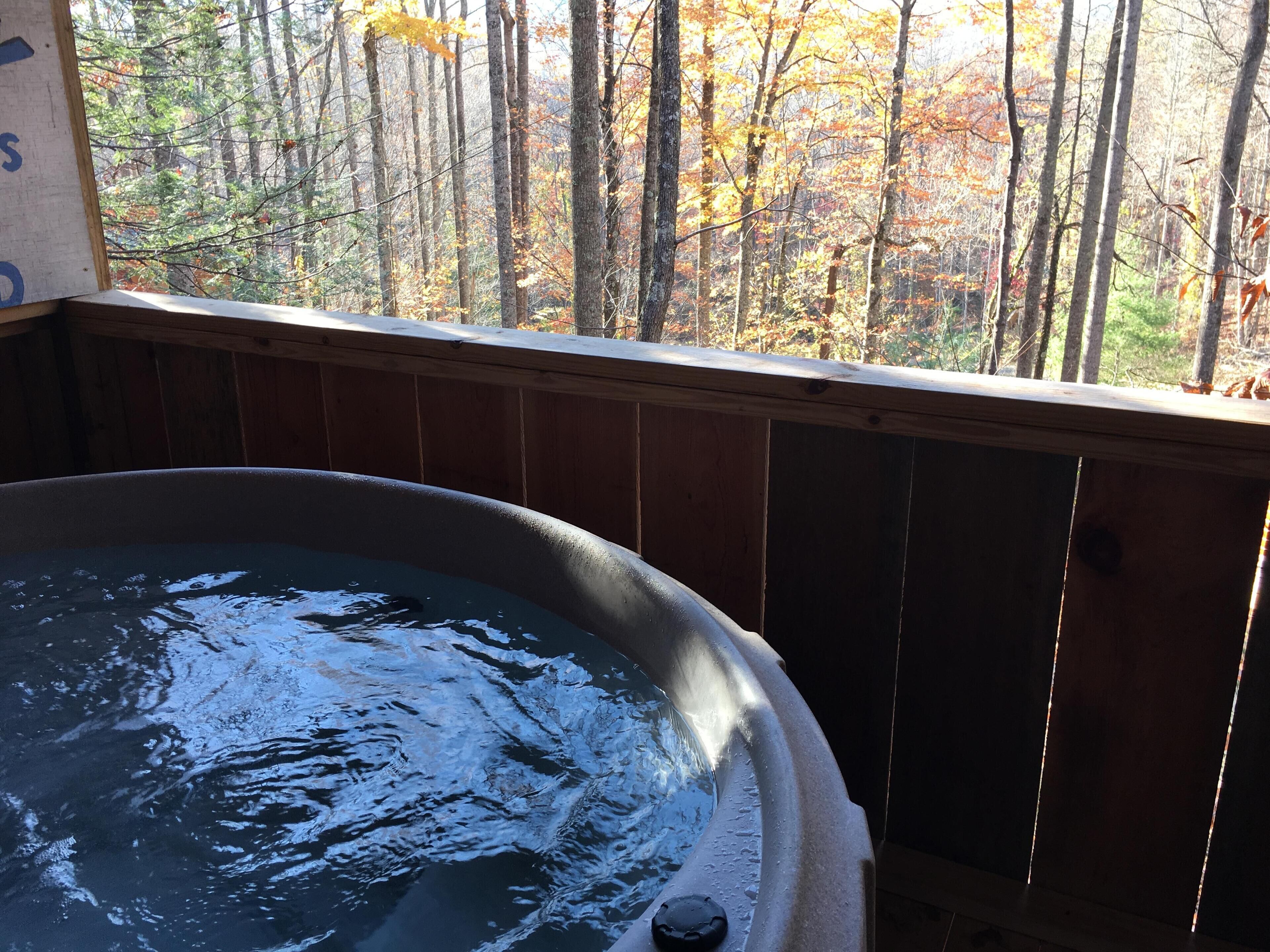 A hot tub with a wooden deck and a view of autumn trees.