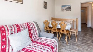 Ett mysigt vardagsrum med en röd och vit mönstrad soffa, ett matbord i trä med stolar och en taklampa.