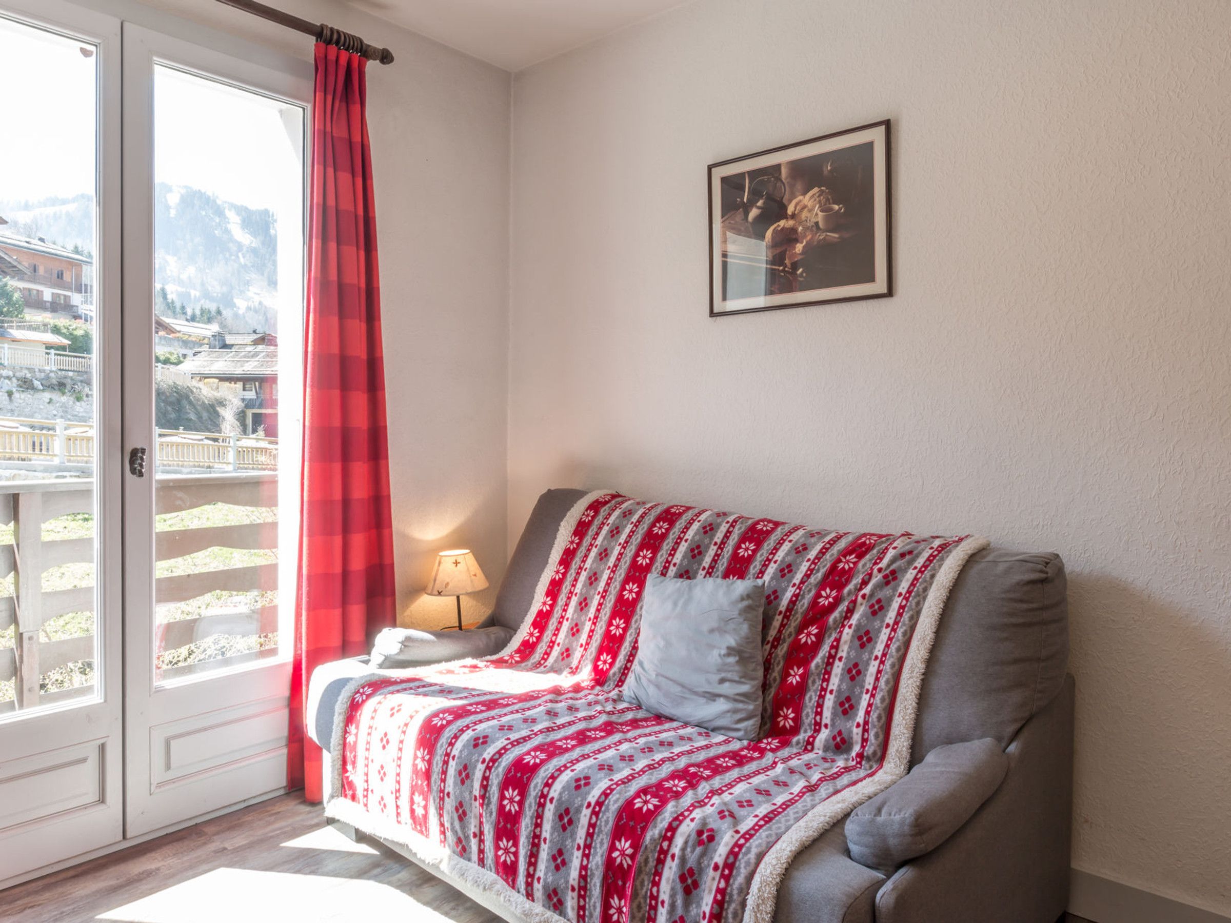 Una habitación acogedora con sofá, lámpara y ventana con cortina roja.