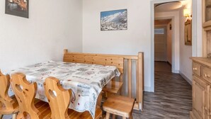 Ett rum med en säng i trä, ett bord med stolar, en målning av ett berg och ett skåp i trä.