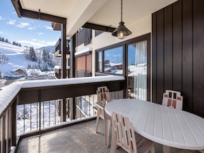 A balcony with a table and chairs, overlooking a snowy landscape with buildings.