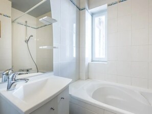 Un baño moderno con una bañera blanca grande, zona de ducha separada y tocador con lavamanos y espejo.
