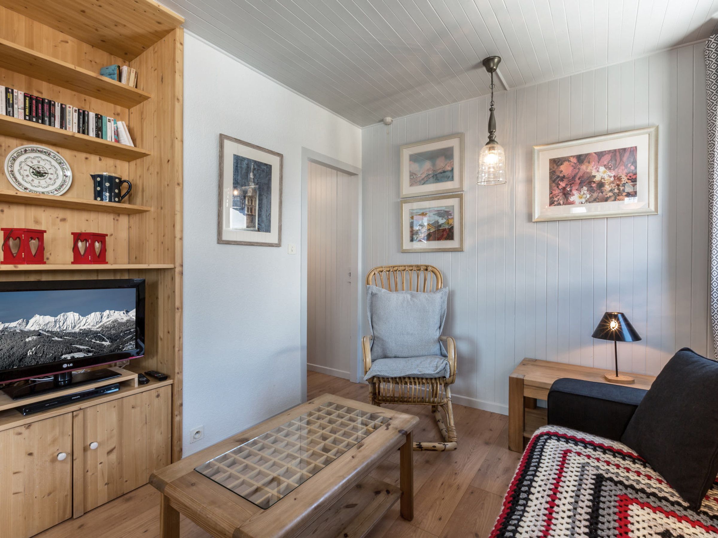 Una sala acogedora con un mueble bajo para el televisor de madera, un sillón de mimbre, una mesita y un sofá.