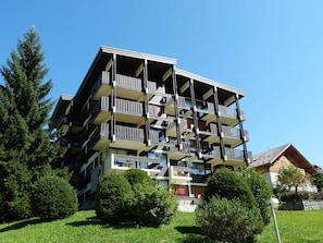 A multi-story building with balconies, surrounded by greenery and trees.