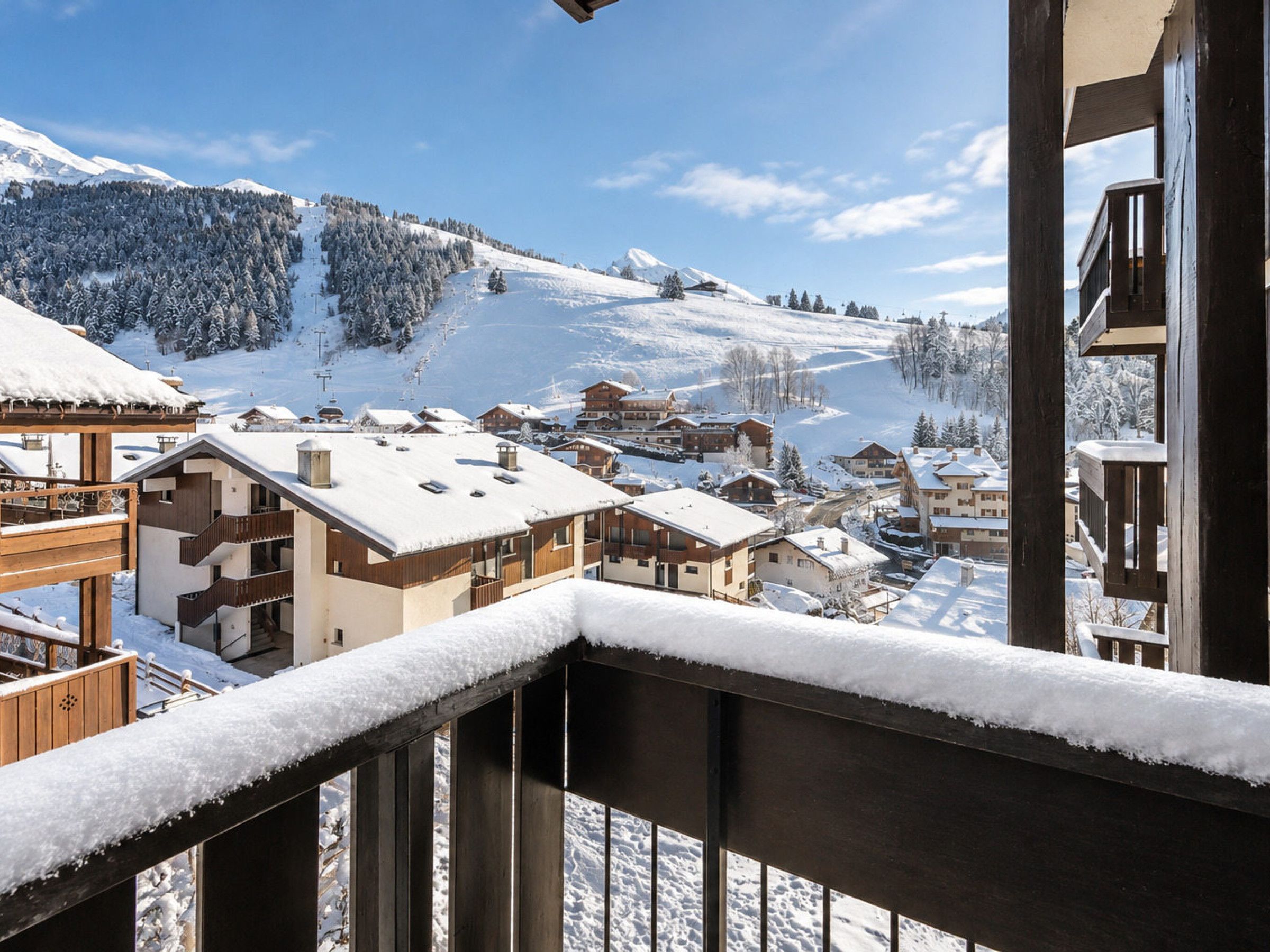 A snow-covered mountain village with chalet-style buildings, a ski lift, and a clear sky.