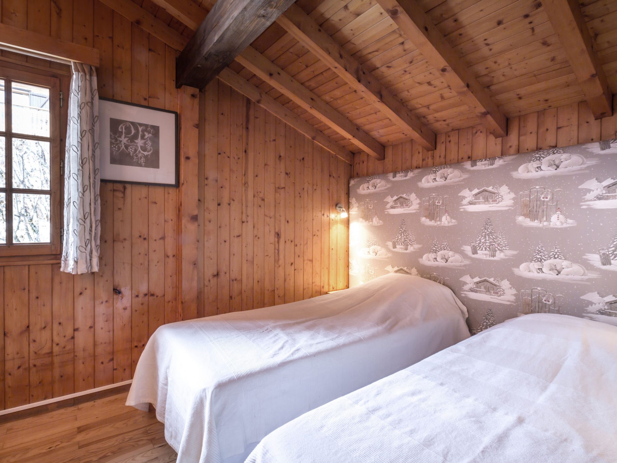 A wooden room with two beds, a window with a curtain, and a wall with a patterned wallpaper.