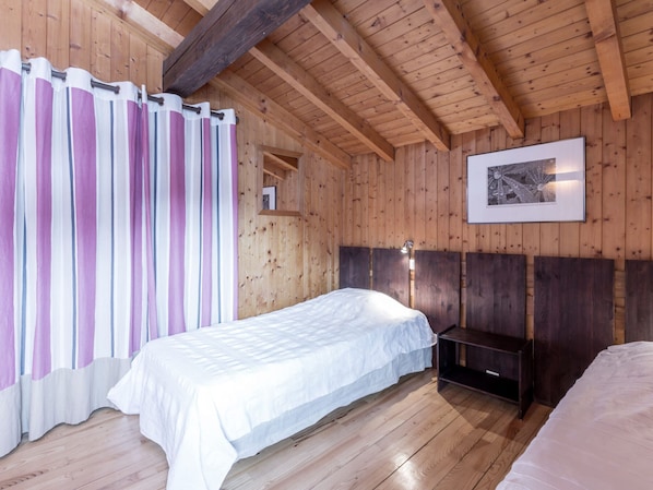 A wooden cabin room with a bed, a bedside table, a hanging light, and a framed picture on the wall.