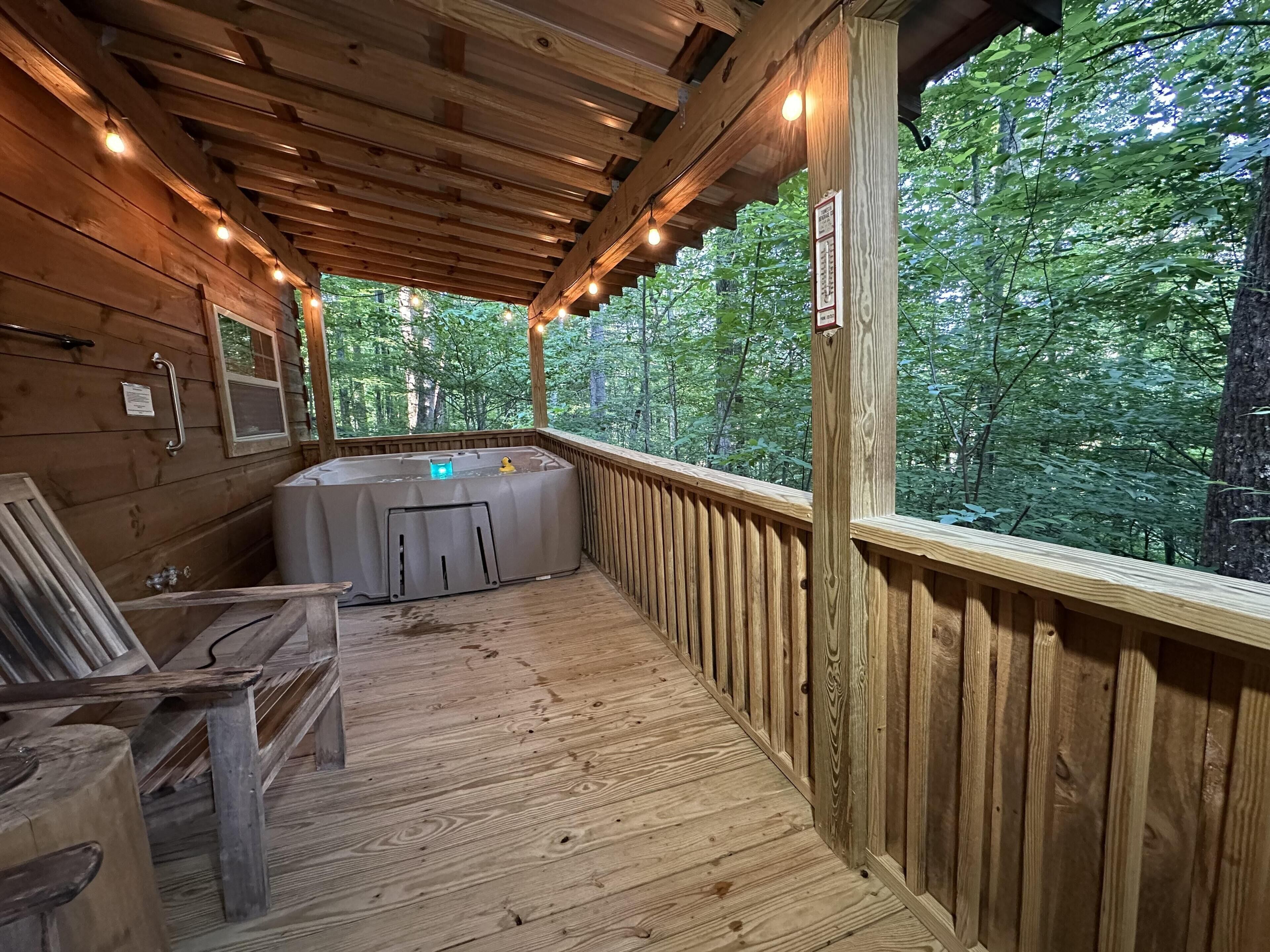 A wooden deck with a hot tub, wooden railings, and a view of a forest.