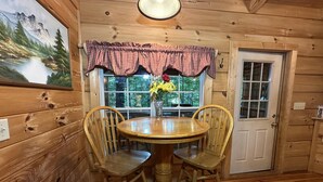 A wooden interior with a round table, two chairs, a door, and a window with a view of trees. - “Lovey Dovey: Your Romantic Asheville Cabin Escape” (Asheville)
