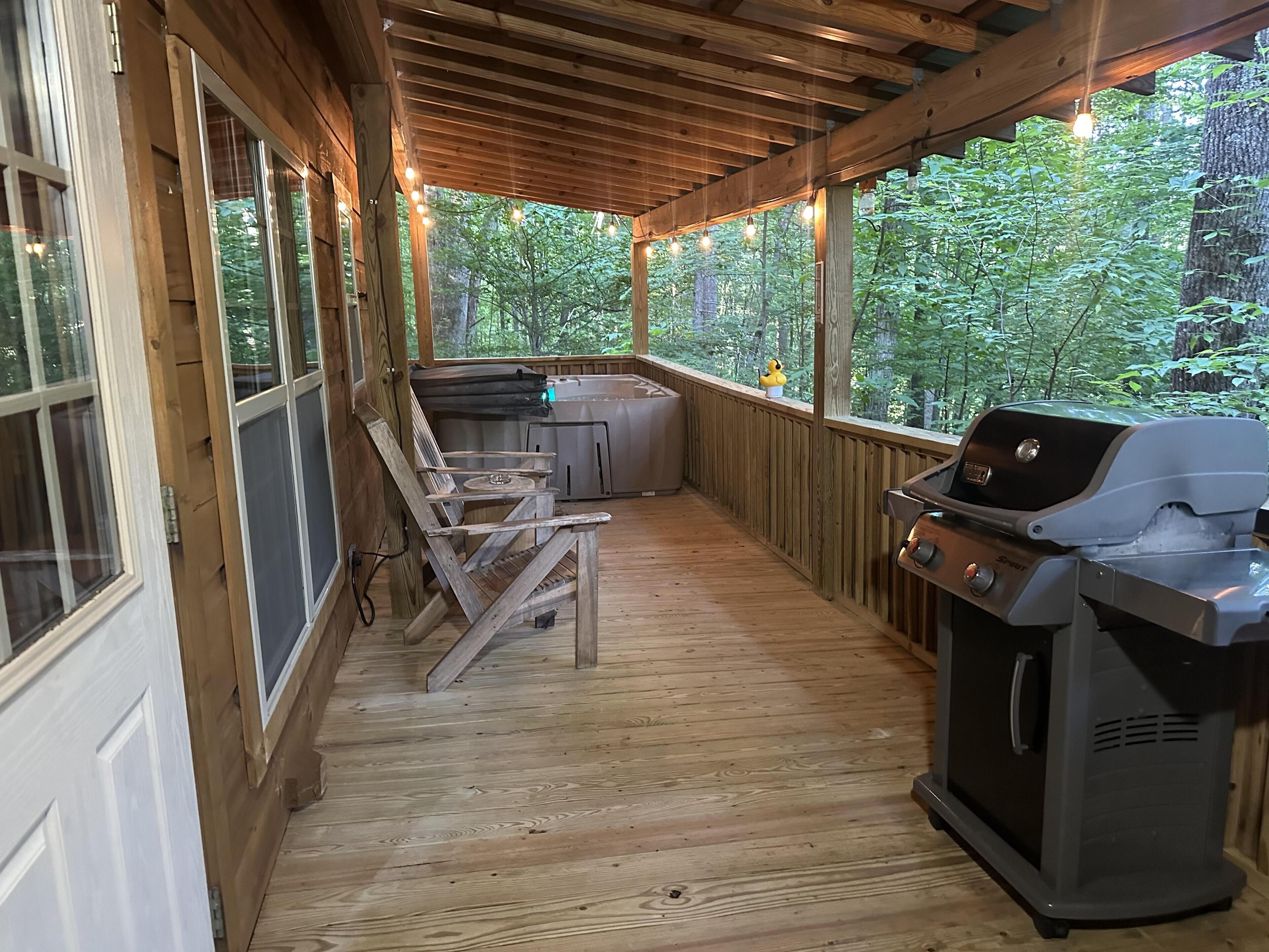A covered outdoor area with a grill, seating, and a hot tub.