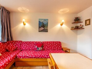 A red sofa with a mountain painting above it, two wall-mounted lamps, a small table, and a shelf with decorative items. - Studio with balcony, pets allowed, near slopes and shops (La Clusaz)