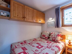 Un dormitorio con cama, armarios de madera, una lámpara de pared, un cuadro enmarcado y una ventana con cortinas.