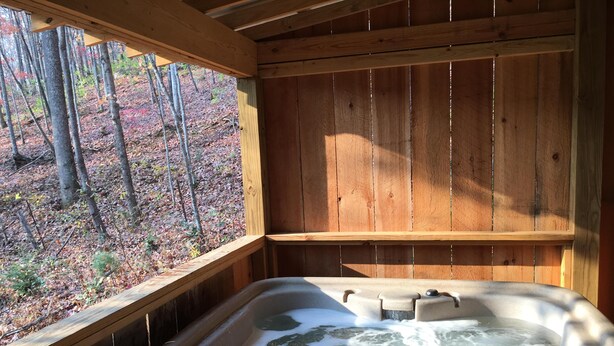 A wooden cabin with a hot tub and a window overlooking a forest.