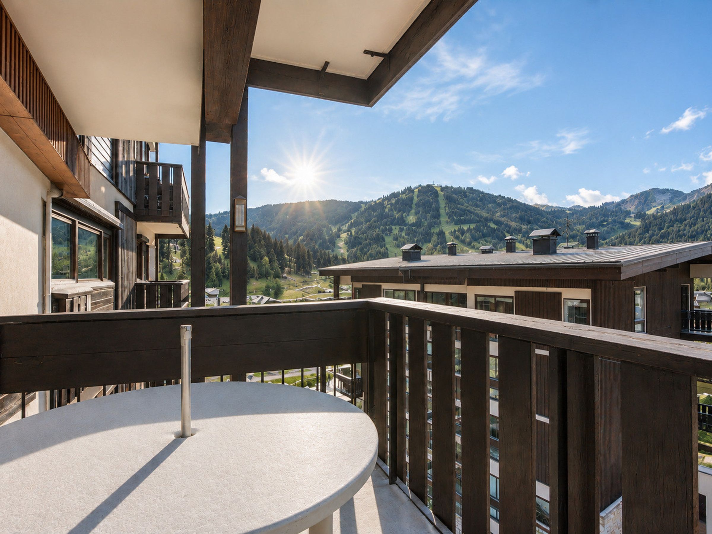 A balcony with a round table, wooden railings, and a view of a mountain landscape.