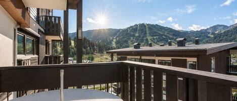 A balcony with a round table, wooden railings, and a view of a mountain landscape.