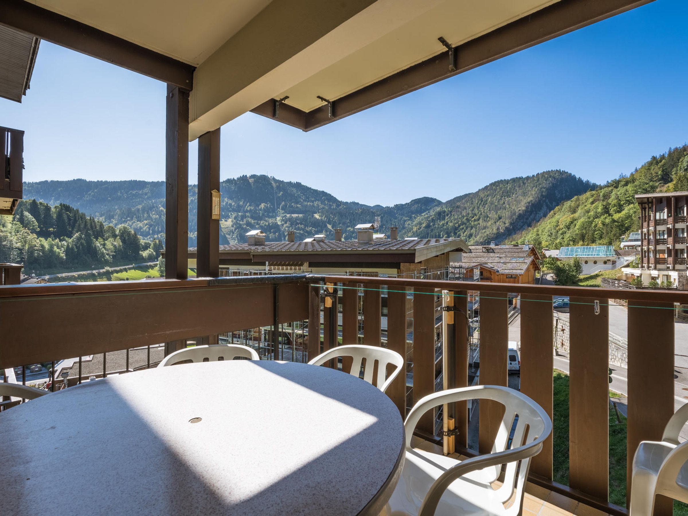 Un balcon avec une table et des chaises, donnant sur un paysage montagneux parsemé de bâtiments.