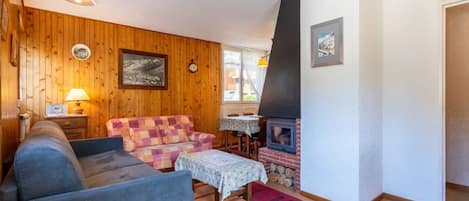 Een gezellige woonkamer met een blauwe bank, een gestreept fauteuil, een klein tafeltje met een lamp en een houtkachel.