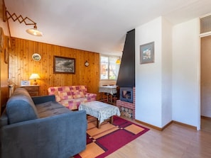 Ein gemütliches Wohnzimmer mit einem blauen Sofa, einem gemusterten Sessel, einem kleinen Tisch mit einer Lampe und einem Kaminofen.