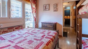 A bedroom with a wooden ceiling, a bed with a patterned quilt, a dresser, and a view of the outside balcony. - 3* Apartment in La Clusaz, 5 guests, parking (La Clusaz)
