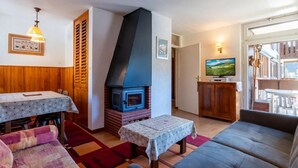 A cozy living room with a fireplace, a sofa, a dining table, and a television. - 3* Apartment in La Clusaz, 5 guests, parking (La Clusaz)