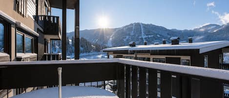 A balcony with a snow-covered table, a view of snow-covered mountains, and a clear sky.