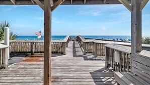 A wooden boardwalk leading to a beach with an American flag and a wind turbine in the distance. - DIRECT GULF FRONT UNIT, CHARMING FIRST FLOOR LOCATION, TONS OF FAMILY AMENITIES, (Orange Beach)