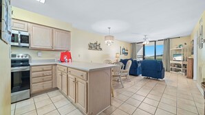 A spacious kitchen with wooden cabinets, a central island, and a dining area with a blue sofa and chairs. - DIRECT GULF FRONT UNIT, CHARMING FIRST FLOOR LOCATION, TONS OF FAMILY AMENITIES, (Orange Beach)