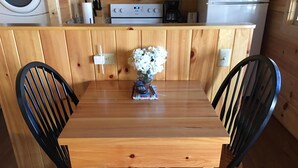 Una mesa de comedor de madera con dos sillas negras, un florero con flores blancas y un control remoto sobre la mesa.