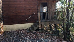 Una cabaña rústica con fachada de madera, un pequeño porche y una escalera que lleva a la entrada.