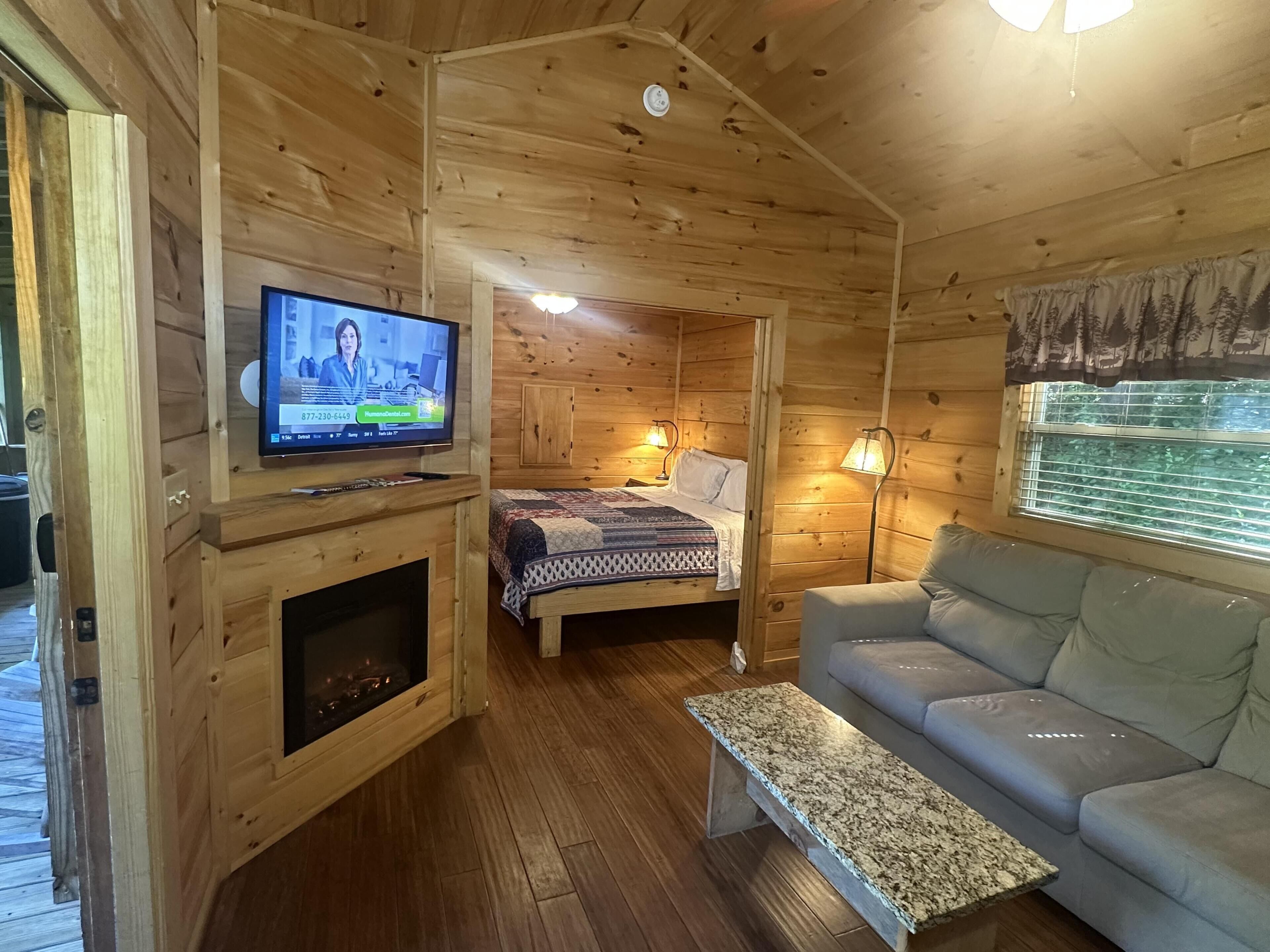 Interior d'una cabana de fusta amb televisió, un llit, un sofà i una llar de foc.