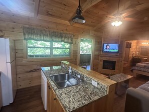 A wooden cabin interior with a kitchen, a dining area, a TV, and a fireplace.