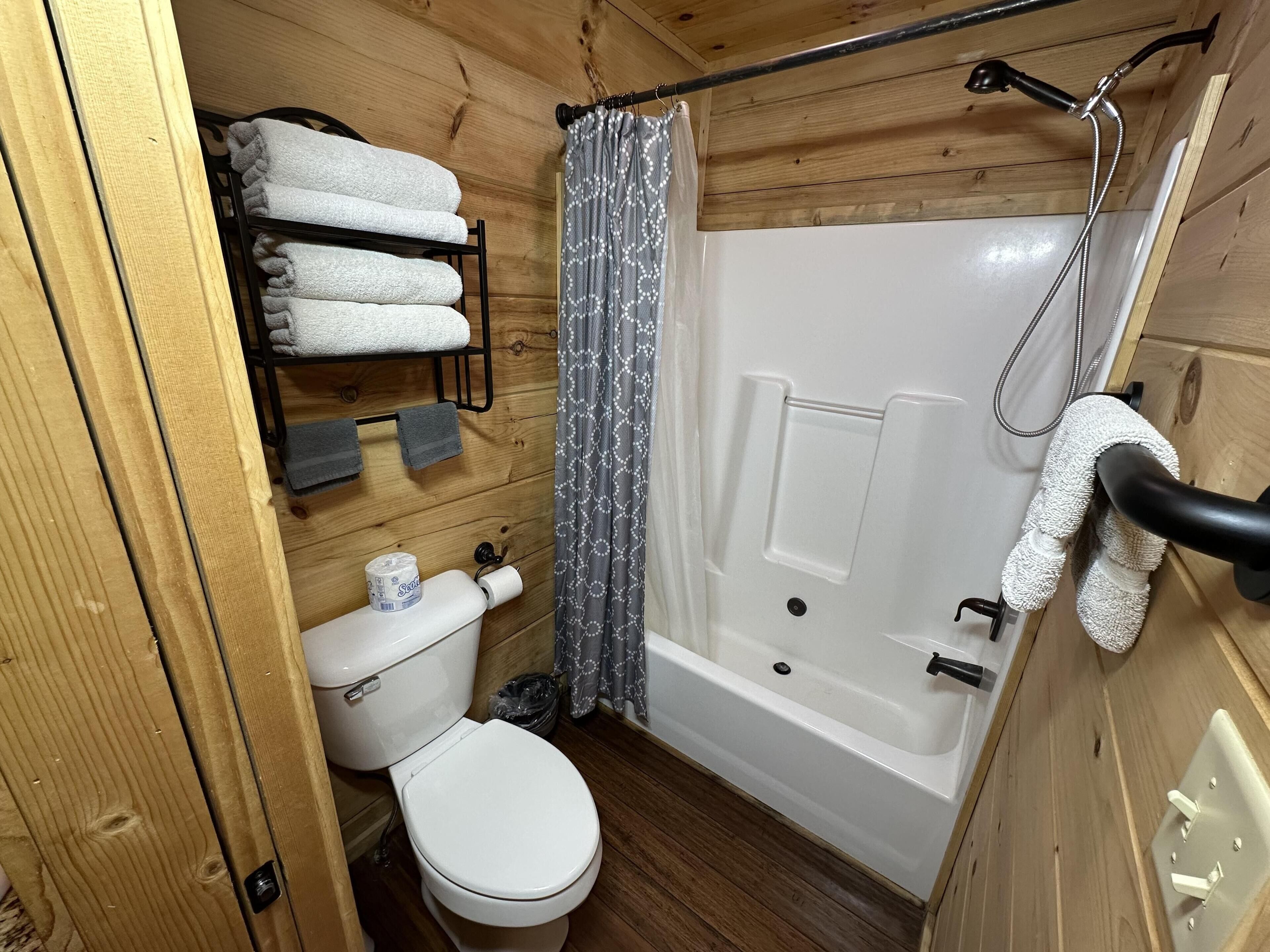 A wooden-paneled bathroom with a toilet, a towel rack with folded towels, a shower curtain, and a bathtub.