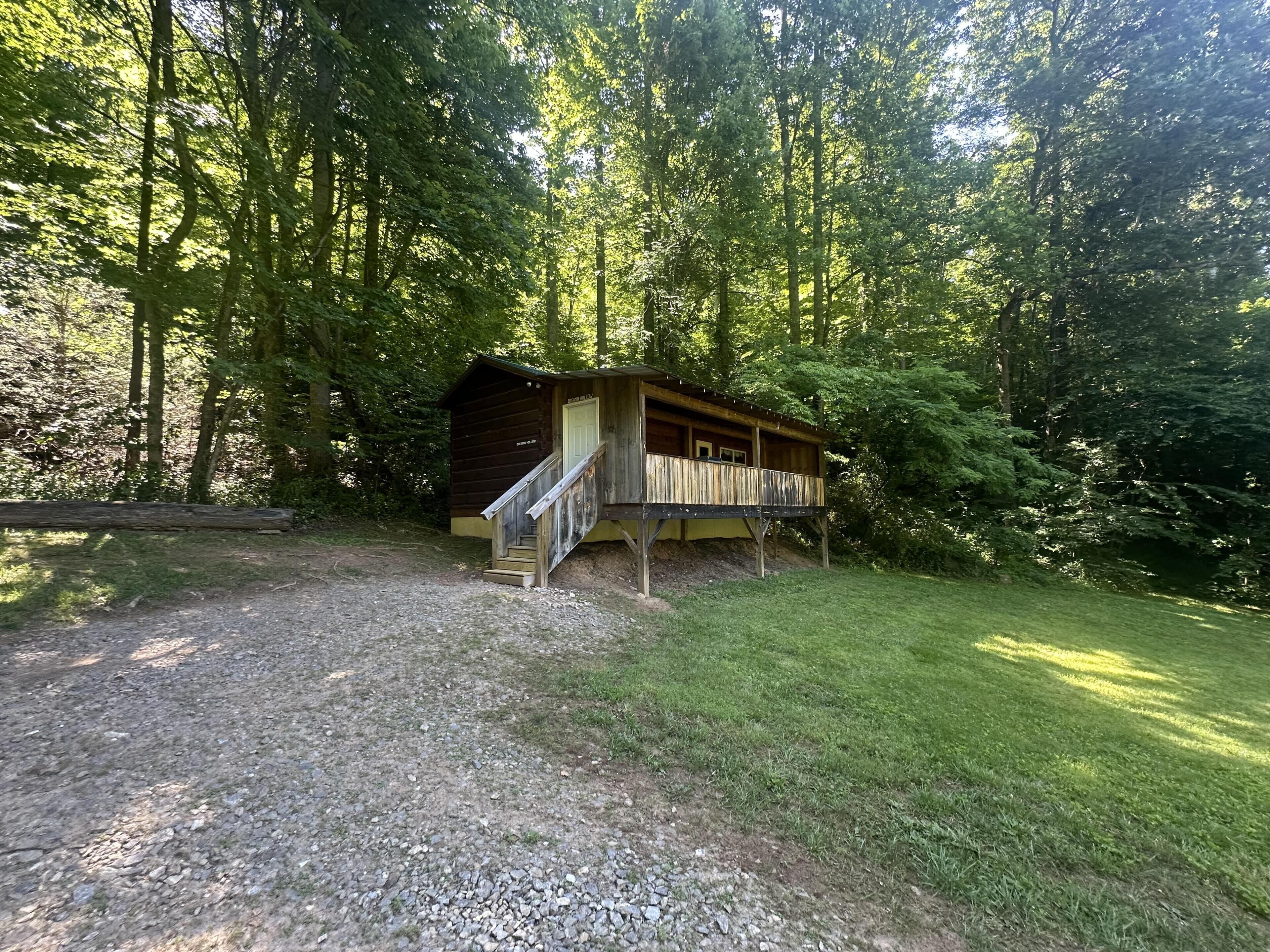 A rustic cabin with a wooden deck, surrounded by dense forest.