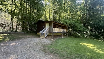 A rustic cabin with a wooden deck, surrounded by dense forest.