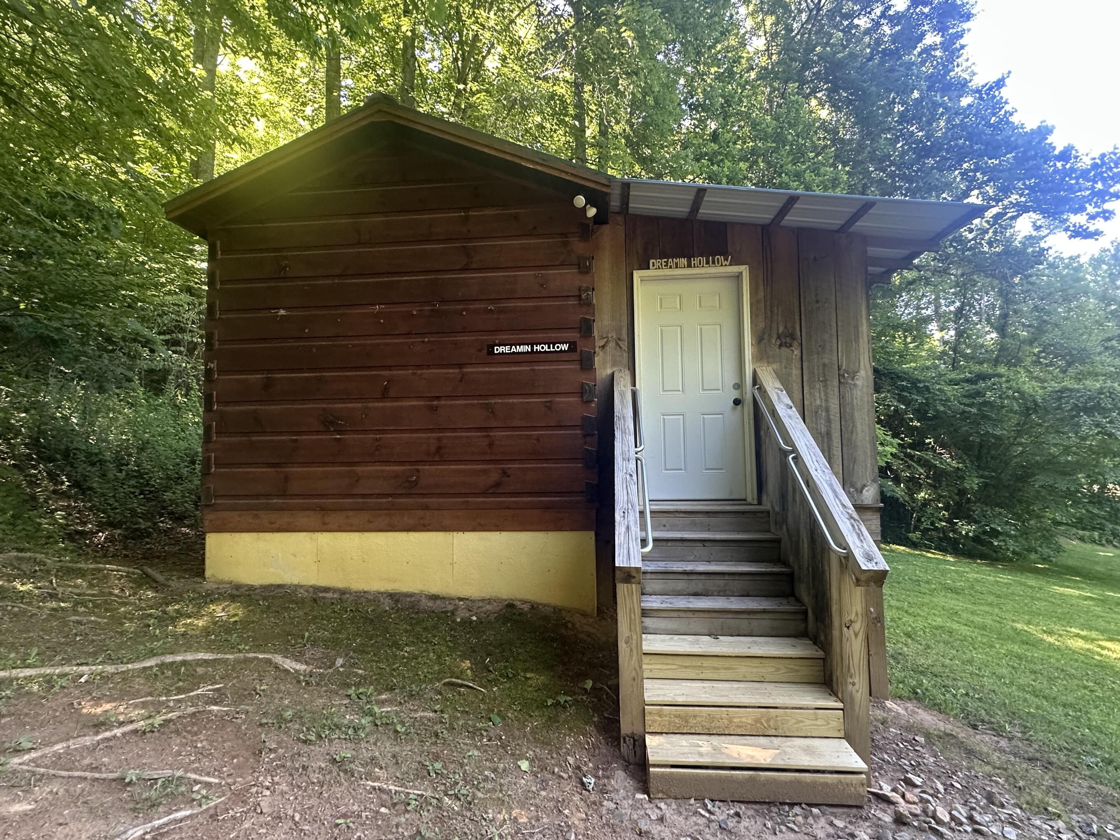 A wooden cabin named 'Dreamin' Hollow' with a single door and a set of wooden stairs leading up to it.